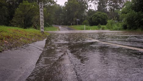 Gold-Coast,-Queensland,-16-February-2024---Low-shot-of-waterflow-into-flooding-across-Hardy's-Road-in-Mudgeeraba-after-heavy-rains-continue-to-lash-South-East-Queensland,-Australia