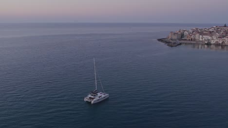 Aerial-view-of-boat-on-calm-sea-with-people-during-sunset,-Cefalu,-Sicily,-Italy