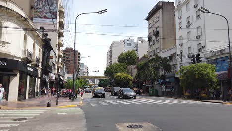 Panoramic-Cityscape-of-Rivadavia-Avenue-in-Buenos-Aires-City-Summer-Daylight-Cars,-taxis-and-asphalt-traffic-driving-by-capital-town-of-Argentina,-Flores-neighborhood