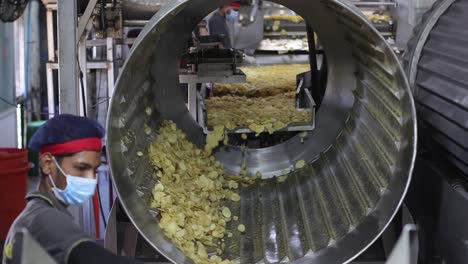 pov-shot-Chips-coming-out-of-the-machine-are-fried-and-men-are-pulling-out-the-bad-chips