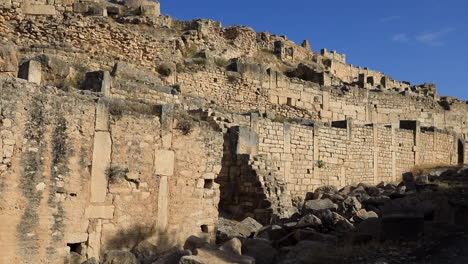 Sunlit-ancient-Roman-ruins-at-Dougga,-stone-walls-and-arches,-clear-sky,-historical-site