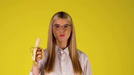 Suggestive-Smart-looking-woman-eats-a-banana-opening-her-mouth-deeply-caucasian-blonde-smiling-girl,-studio-portrait-background,-infinite-yellow-chroma