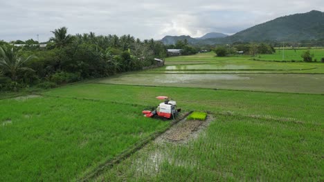 Tractor-Agrícola-Trabajando-En-Los-Exuberantes-Campos-Del-Centro-De-Virac,-Catanduanes,-Filipinas,-Con-Montañas-Como-Telón-De-Fondo