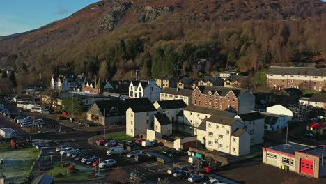 Drone-Descendente-Sobre-El-Pueblo-De-Aberfoyle-Con-La-Colina-Craigmore-Al-Fondo-Que-Se-Revela-En-Escocia