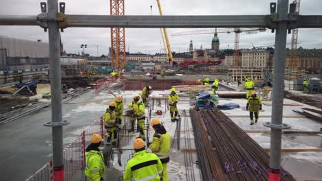 Workers-move-around-at-construction-site-in-Stockholm,-metal-bars-in-foreground