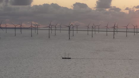 Luftaufnahme-Eines-Segelschiffs-Mit-Einem-Großen-Windpark-Mit-Turbinen-Im-Hintergrund-Bei-Sonnenuntergang,-Ijsselmeer,-Niederlande