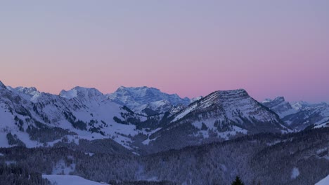 Drone-captured-footage-revealing-the-ethereal-charm-of-sunrise-illuminating-the-silhouette-of-a-snowy-mountain-range