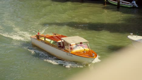 Taxi-boat-on-the-water-of-Canal-Grande-in-Venice,-Italy,-is-cruising-under-a-bridge-in-the-morning-sunlight