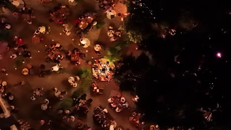 Drone-rises-from-bird's-eye-view-spinning-above-people-gathered-to-eat-at-round-tables-at-night-in-Kura-Hulanda-village-in-Otrobanda-Willemstad-Curacao