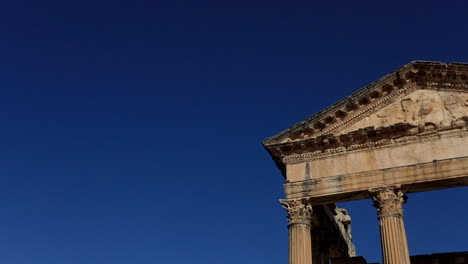 Sunlit-ancient-Roman-ruins-at-Dougga-against-a-clear-blue-sky,-highlighting-historical-architecture