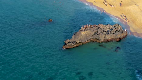Aerial-view-of-People-crowd-on-top-of-rock-formation-jumping-into-water-at-Waimea-Bay-Beach,-Oahu-Island