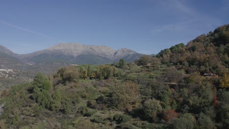 Vuelo-Ascendente-Con-Efecto-Sorpresa-En-Un-Valle-Descubriendo-Un-Entorno-Rural-Con-Una-Población-Y-Montañas-Impresionantes-En-Una-Ladera-Con-árboles-Coloridos-En-Otoño-Y-Una-Carretera-Con-Coches-ávila-España