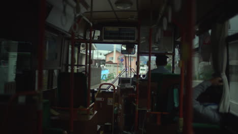 As-the-bus-travels-through-Fujikawaguchiko,-red-tube-railings-catch-our-eye-from-the-window,-while-inside,-a-uniformed-conductor-carefully-navigates-the-journey-forward