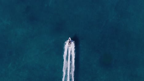 Top-down-tracking-aerial-follows-speed-boat-and-white-wash-wake-in-cerulean-blue-ocean-water