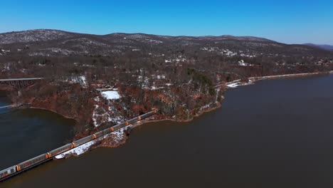 An-aerial-view-of-a-long-cargo-train-traveling-along-the-Hudson-River-on-a-sunny-day-with-clear-blue-skies