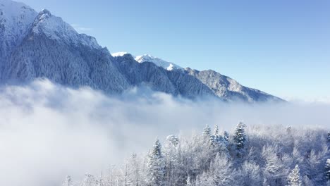 Snow-capped-Bucegi-Mountains-rising-above-clouds-with-a-serene-sky,-winter-landscape