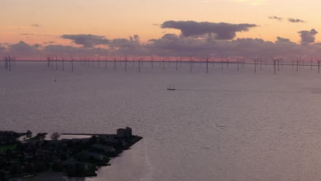 Luftaufnahme-Eines-Segelschiffs-Mit-Einem-Großen-Windpark-Mit-Turbinen-Im-Hintergrund-Bei-Sonnenuntergang,-Ijsselmeer,-Niederlande