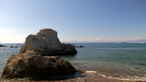 Low-angle-ocean-shot-with-rocks-and-Mount-Fuji-with-snow-top-in-distance