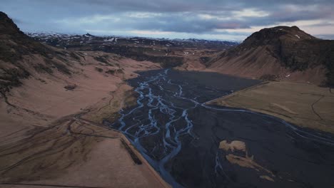 Aerial-landscape-view-of-a-river-flowing-in-a-mountain-valley,-in-Iceland,-on-a-moody-day