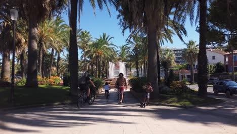 Families-with-bikes-and-scooters-move-in-park-with-fountain-in-Antibes
