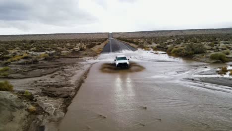 Camioneta-Blanca-Conduciendo-Por-Una-Carretera-Fangosa-E-Inundada-En-El-Desierto