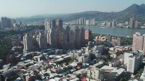 Aerial-View-of-Zhuwei,-Taipei-City-Skyline-With-River-and-Mountains-in-the-Background