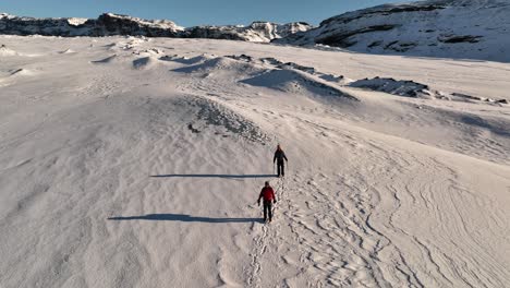 Aerial-panoramic-view-over-two-people-hiking-on-a-expedition-on-Sólheimajökull-glacier,-in-Iceland