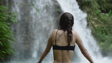 Hermosa-Mujer-En-Bikini-Negro-Mira-Fijamente-A-La-Hermosa-Cascada-Tropical-En-El-Bosque