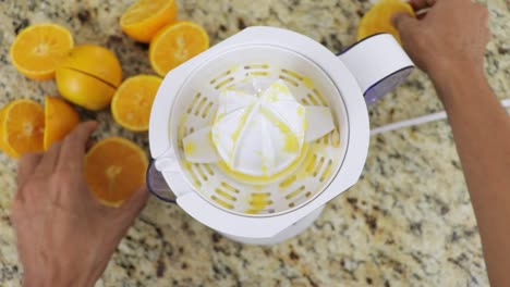 Squeezing-fresh-orange-juice-with-a-machine-in-kitchen,-first-person-view