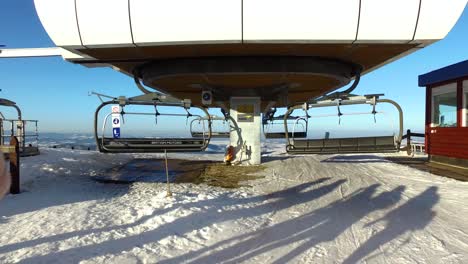 Ski-chair-lift-exit-at-top-of-winter-sport-resort-mountain,-sunny-day