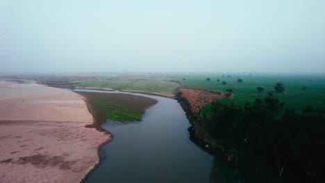Fluss-Schlängelt-Sich-Durch-Eine-Grüne-Landschaft-Im-Morgengrauen,-Neblige-Luft,-Luftaufnahme