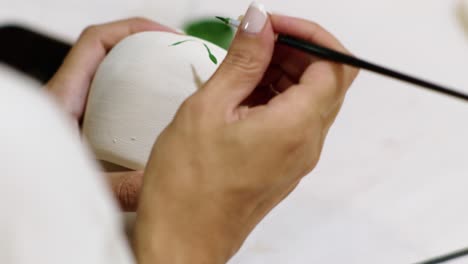 Close-up-of-the-hands-of-an-artist-painting-a-drawing-on-the-pottery-in-a-workshop