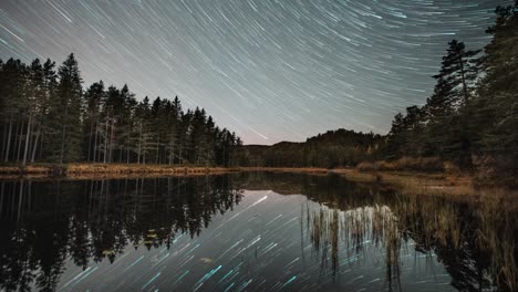Starry-night-sky-with-star-trails-reflected-in-the-still-surface-of-the-dark-lake-in-a-timelapse-video