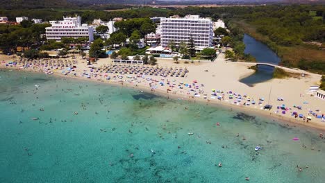 Toma-De-Drones-Acercándose-A-La-Costa-De-La-Playa-De-Canyamel,-Ubicada-En-La-Isla-De-Mallorca,-Y-A-La-Isla-Frente-A-La-Costa-De-España-En-El-Mar-Mediterráneo.