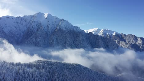 Snow-capped-Bucegi-Mountains-towering-above-clouds,-serene-winter-landscape