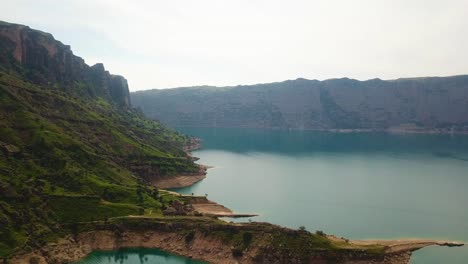 Scenic-landscape-of-dam-lake-in-spring-season-rock-cliff-green-pasture-meadow-covered-in-a-cloudy-weather-in-Iran-Dezful-the-mountain-hill-landscape-sea-marine-adventure-travel-to-coastal-green-ocean