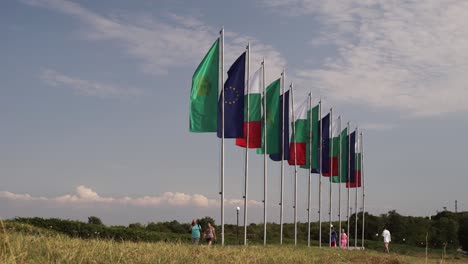Tourists-and-visitors-walking-by-row-of-flags-outside-Bulgarian-State-Monument