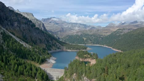 Lago-di-devero-in-alpe-devero-with-clear-waters-surrounded-by-alpine-trees-and-rugged-mountains,-aerial-view