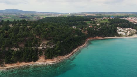 Toma-Aérea-De-La-Costa-Con-Pinos-Y-Aguas-Turquesas-En-Kallithea,-Halkidiki,-Grecia