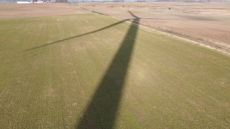 Schatten-Einer-Riesigen-Windmühle,-Die-Sich-Auf-Einer-Feldwiese-Dreht,-Sonniger-Tag,-Luftaufnahme