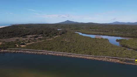 Aerial-views-of-Urunga-boardwalk-along-the-banks-of-the-Kalang-River,-to-the-junction-with-the-Bellinger-River-and-out-to-the-ocean