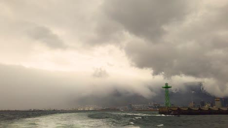 Imágenes-En-Primera-Persona-Desde-La-Parte-Trasera-De-Un-Barco-Lleno-De-Nubes-De-Tormenta-Sobre-Ciudad-Del-Cabo-Mientras-Pasa-Un-Barco-Costero