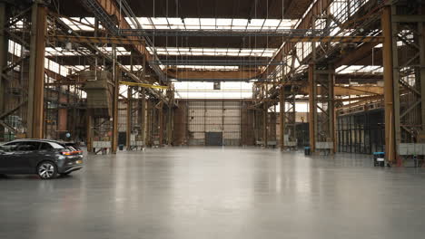 Silver-SUV-slowly-driving-out-of-huge-empty-industrial-warehouse-storage-hangar