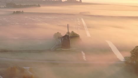 Aerial-view-of-traditional-old-windmill-in-a-meadow-with-low-fog-at-sunrise,-Friesland,-Netherlands
