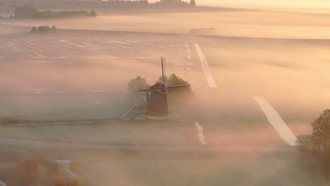 Vista-Aérea-Del-Antiguo-Molino-De-Viento-Tradicional-En-Un-Prado-Con-Niebla-Baja-Al-Amanecer,-Frisia,-Países-Bajos