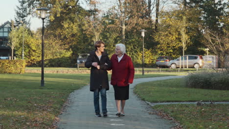 Elderly-mother-walking-together-with-mature-daughter-outside-on-path