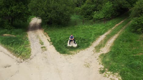 Retreating-drone-shot-from-a-tourist-that-can-be-seen-sitting-on-a-rock-landmark-in-the-middle-of-a-crossroad-in-the-village-of-Tsarichina-Hole-in-Bulgaria
