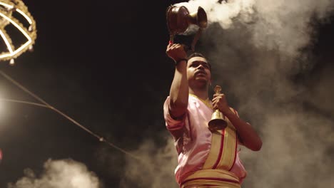 Low-angle-view-of-a-Hindu-priest-performing-religious-Aarti-at-night-beside-Ganges-river-in-Varanasi,-India