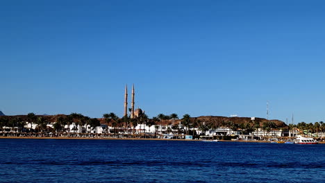 Calm-waterfront-view-of-the-Sahaba-Mosque-in-Sharm-El-Sheikh-under-clear-blue-skies,-static-shot