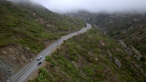 Santa-Monica-Mountains-in-Malibu,-California-on-cloudy-day-with-traffic-driving-on-road-and-drone-video-moving-forward-up-high
